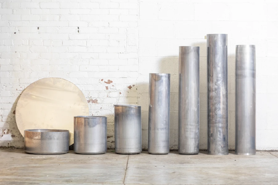 Spun metal cylinders of varying heights beside a circular metal blank, made by Buckeye Shapeform for defense applications.